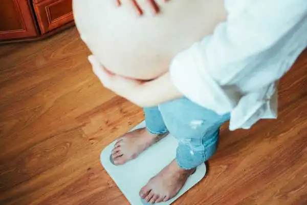 Image of woman weighing herself and experiencing weight gain through pregnancy Northfield